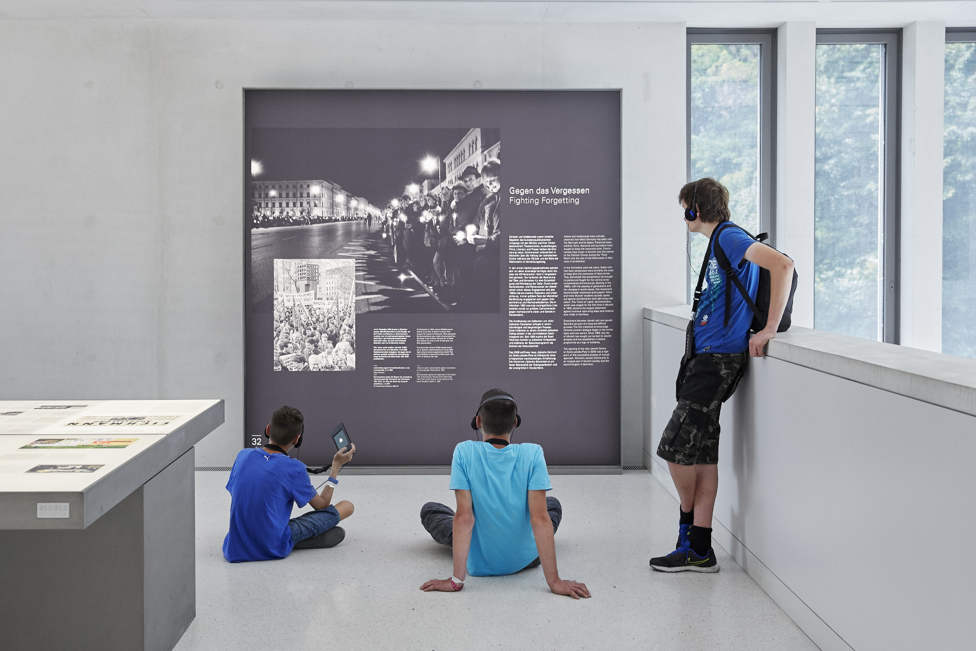 大きな展示パネルを自由な姿勢で眺める3人の若い見学者。