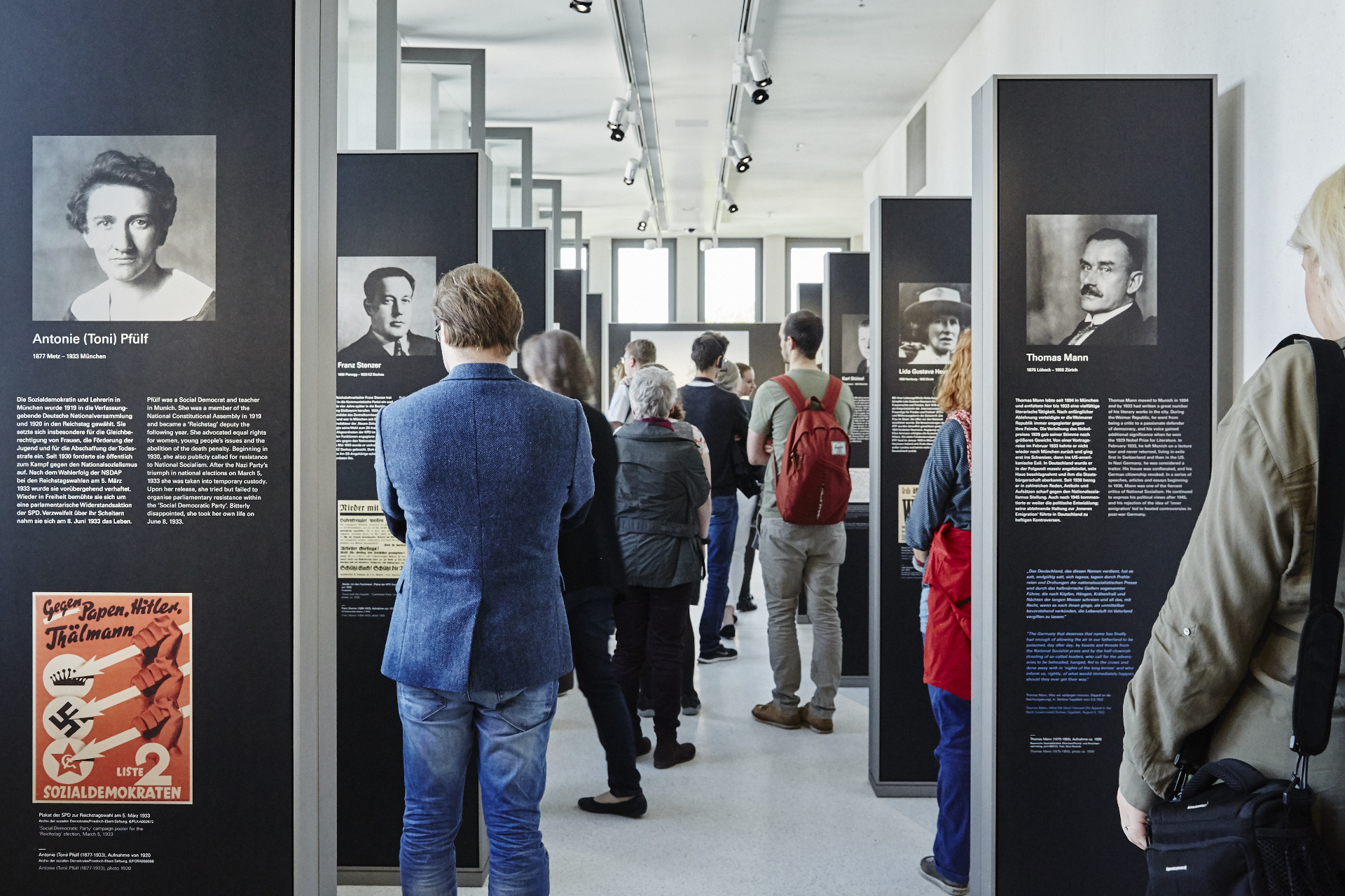 文章や歴史的な写真が掲載された展示パネルを見る多くの来館者。